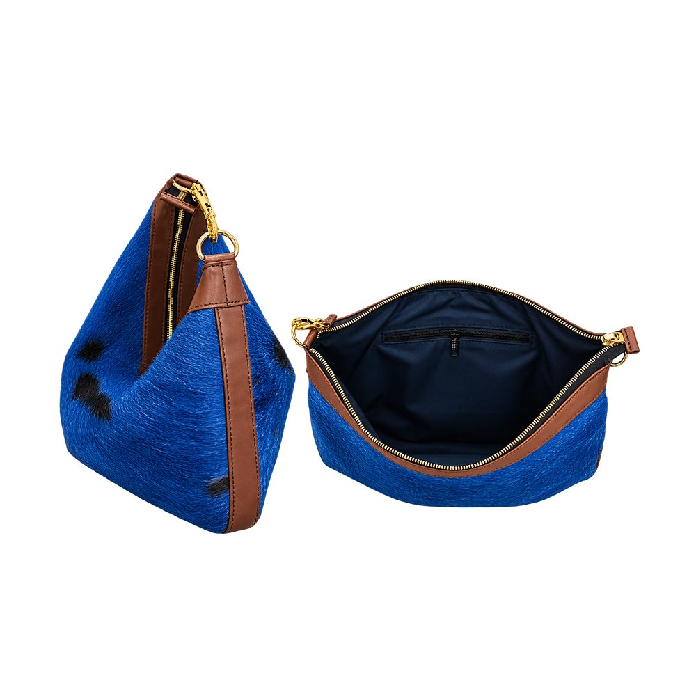 Royal blue hair-on-hide shoulder bag with black patches, brown leather trim, gold-tone zipper, and navy interior lining.